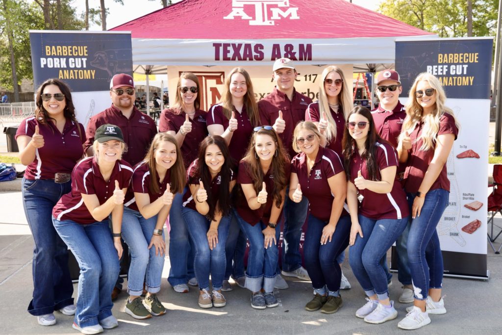 a group of students in Texas A&M polo shirts posing in front of a Texas A&M tent