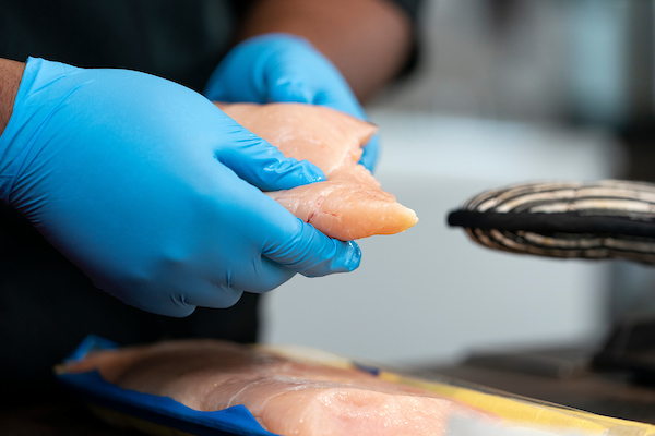 gloved hands holding an uncooked chicken breast