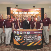 Group of people standing in front of BBQ Genius Counter sign and behind an Agriculture and Life Sciences desk. 