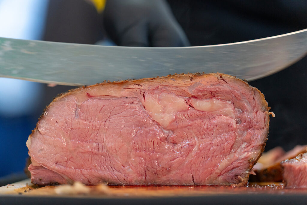 Close up of freshly cooked prime rib on cutting board being cut with knife.