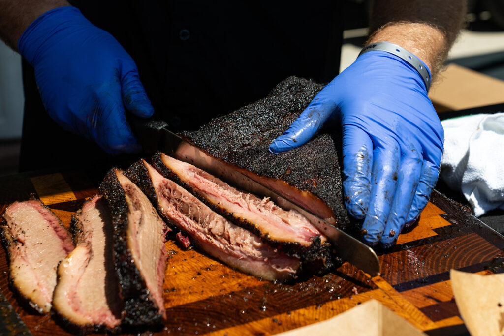 Gloved hands slicing into a smoked brisket on a wooden cutting board