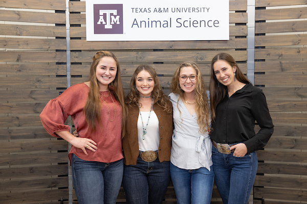 Four female students posing in front of a Texas A&M Department of Animal Science banner.