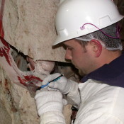 A man is closely inspecting a piece of meat. Is making marking on it with a pencil. 