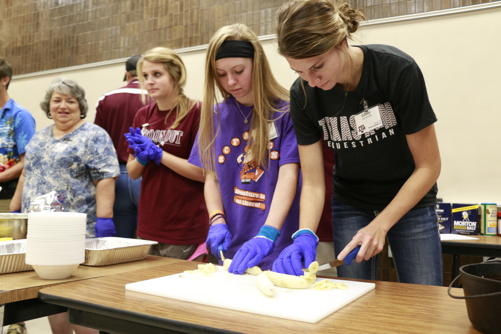 Two girls cutting a banana on a white cutting board. 