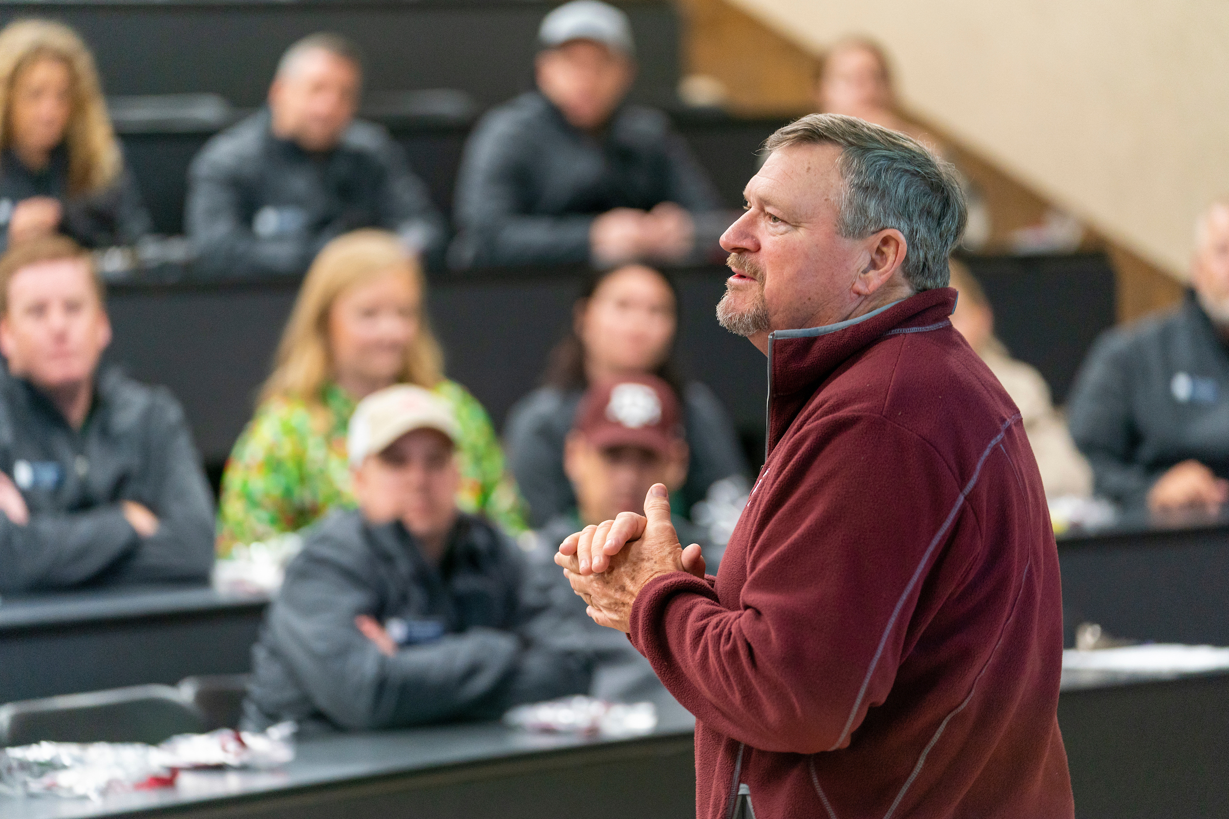 Man speaks at front of filled classroom.