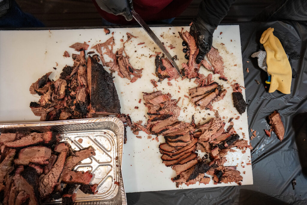 A brisket being cut over a white cutting boards by a person using black gloves. 