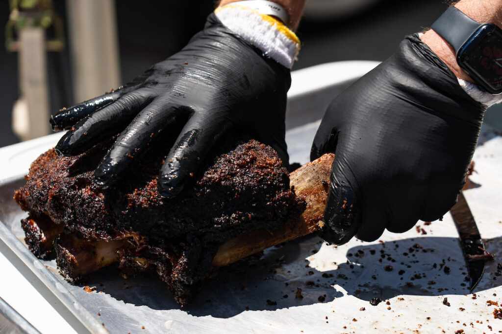 Someone handling a piece of BBQ using black gloves. 