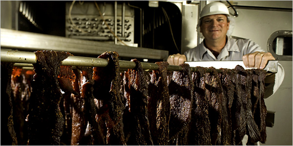 Man in hard hat and lab coat with hanging rack of beef jerky.