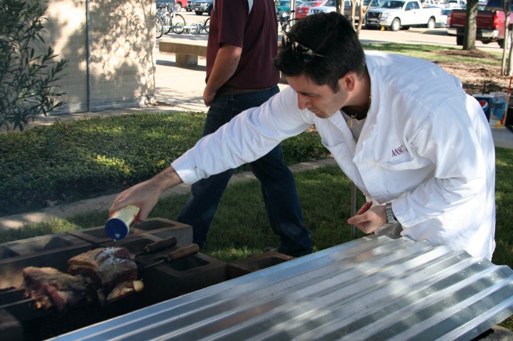 Man in white lab coat putting salt to meat that is cooking. 